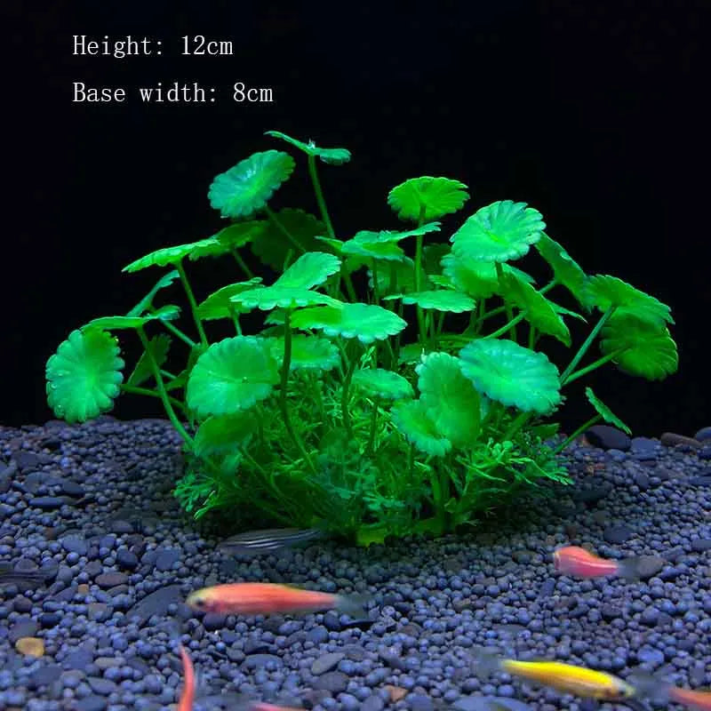 A vibrant green artificial plant with large leaves is placed on dark gravel, featuring a small orange fish nearby.