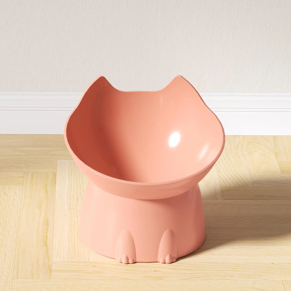 A pink elevated cat bowl with a storage and anti-tip base sitting on a wooden floor.