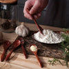 A set of six wooden tea and coffee spoons resting on a woven mat with a garlic bulb and white powder.