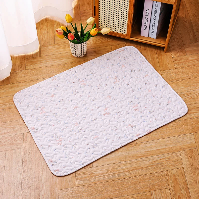 A rectangular white mat with a quilted pattern rests on a light wood floor next to a plant and a wooden shelf.