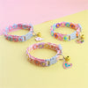 A pink and purple rainbow flower cat collar with a bell is displayed on a light yellow background.