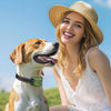 A smiling woman wearing a straw hat is interacting with a dog while demonstrating an electric training collar.