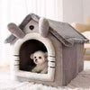 Tente grise pour animal avec toit en bois et entrée arquée, montrant un petit chiot blanc à l'intérieur.