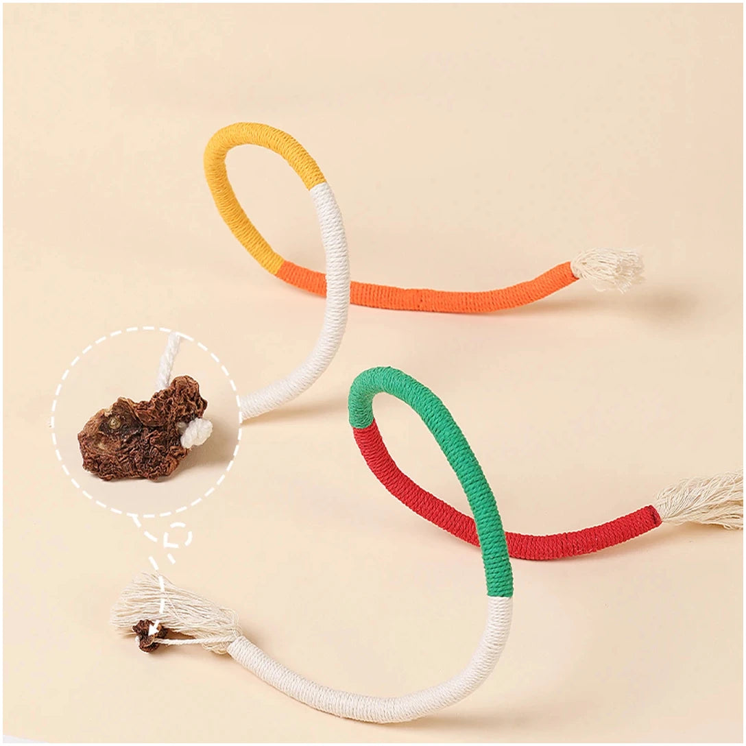 A collection of colorful cotton rope cat toys in orange, white, and green, with a small piece of dark wood visible.