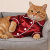 Orangegestromter Kater trägt ein rotes Satin-Pyjama-Oberteil mit weißen Polka-Punkten und einem passenden Kragen.