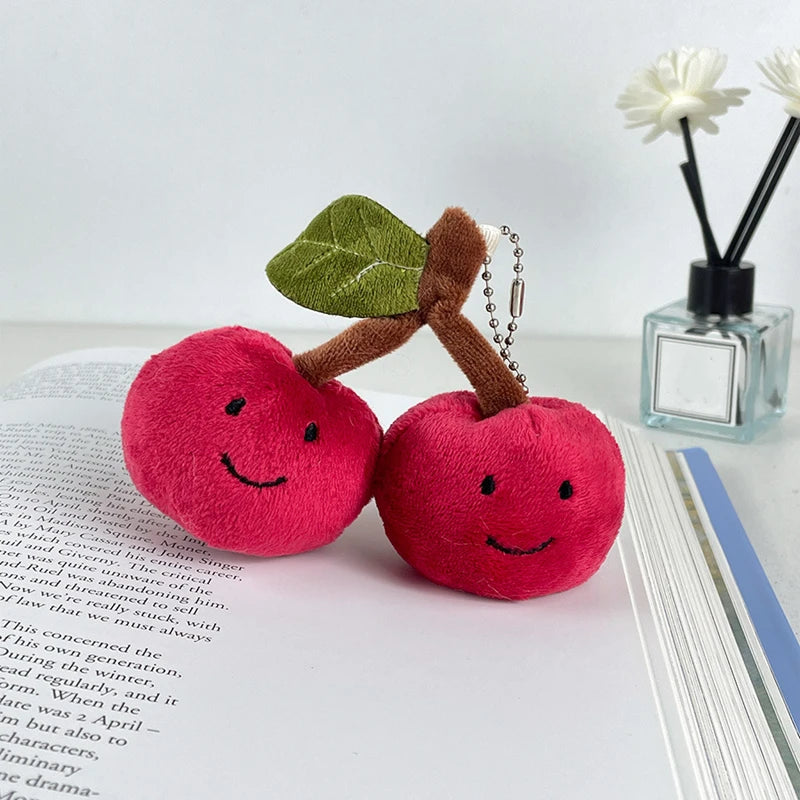 A pair of bright pink cherry plush keychains with green leaves resting on a page of text.