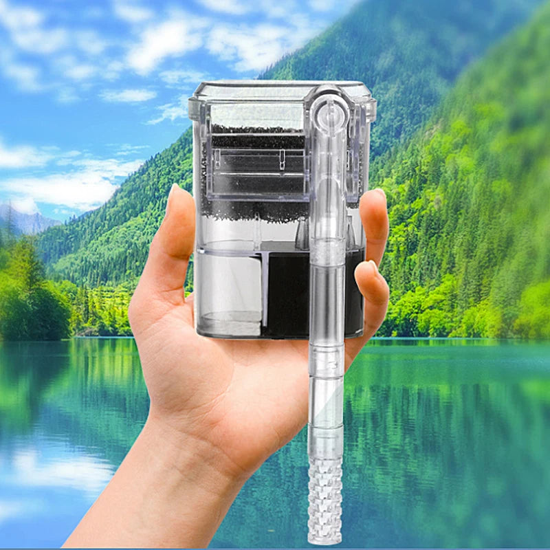 A hand holds a clear USB wall-mount aquarium filter pump with a long tube and filter element against a green, mountainous bac