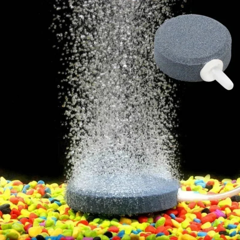 A grey air stone disc is shown dispersing fine bubbles onto a colorful surface for aquarium aeration.
