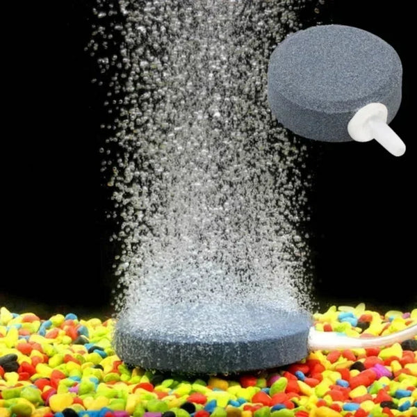 A grey air stone disc is shown dispersing fine bubbles onto a colorful surface for aquarium aeration.