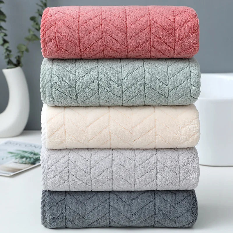 A stack of four plush quick-dry microfiber bath towels in shades of pink, green, cream, and gray.