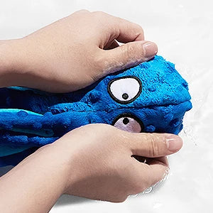 A hand is holding a bright blue squeaky octopus plush dog toy with large eyes and crinkle legs.