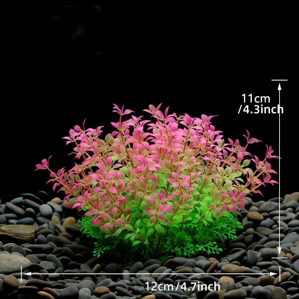A cluster of artificial aquarium plants featuring pink and green foliage planted in dark gravel.