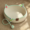 A light green cat scratcher and comfort bed with play balls resting on a tan surface.