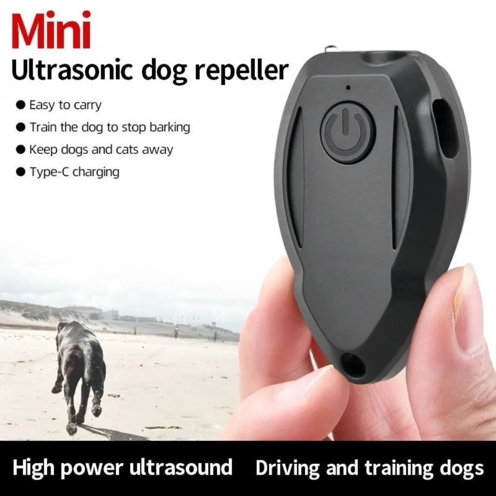 A hand holds a black handheld ultrasonic dog repeller device against a beach background.