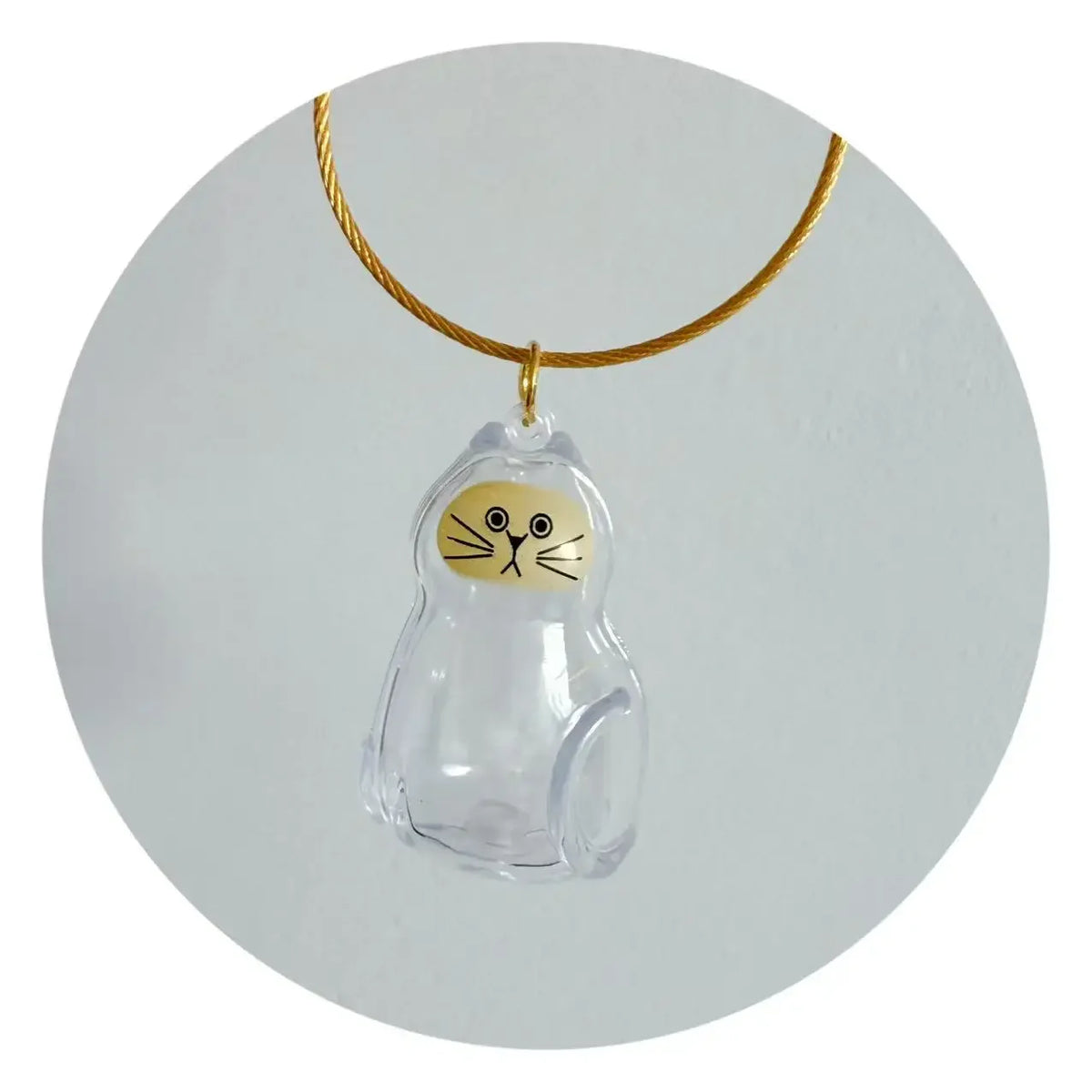 A clear glass charm shaped like a cat's head hangs from a gold-colored cord.