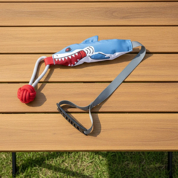 A blue and white shark rope tug toy with a suction cup is laid out on a wooden table.