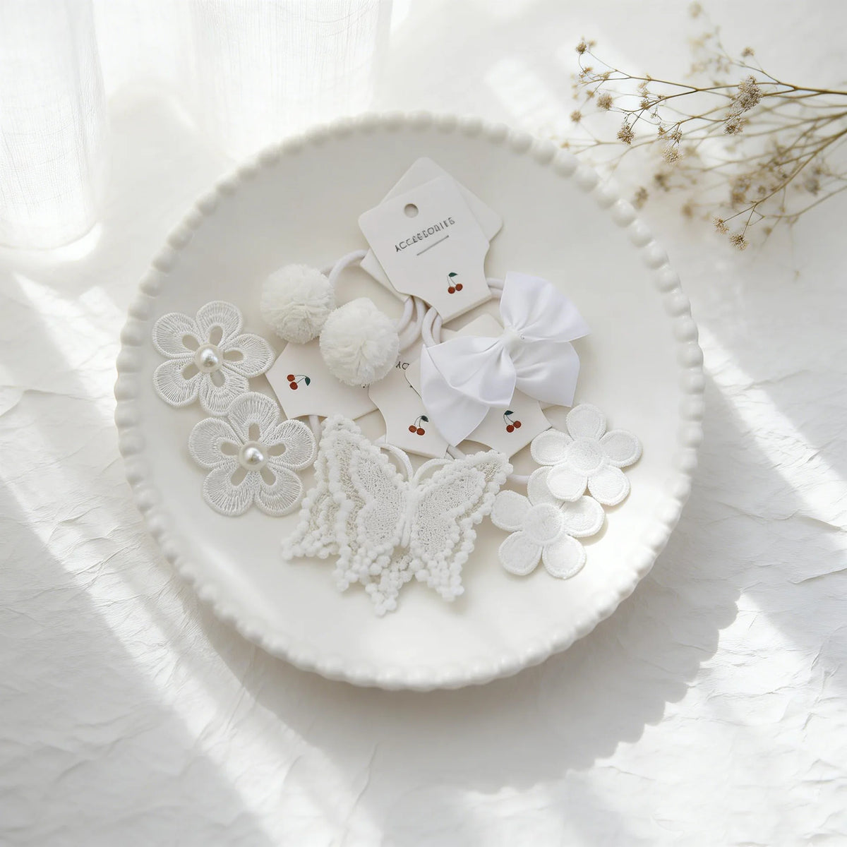 Accessoires pour cheveux en dentelle blanche et pompons, présentés sur une assiette blanche avec une lumière naturelle douce.