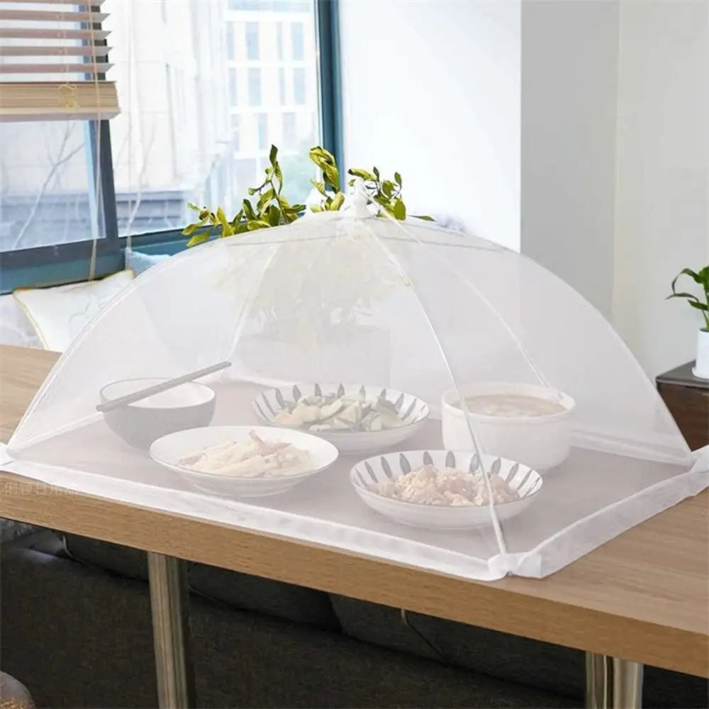 غطاء طاولة شبكي على شكل قبة موضوع على طاولة خشبية، يحمل أطعمة للضيافة أو النزهات.