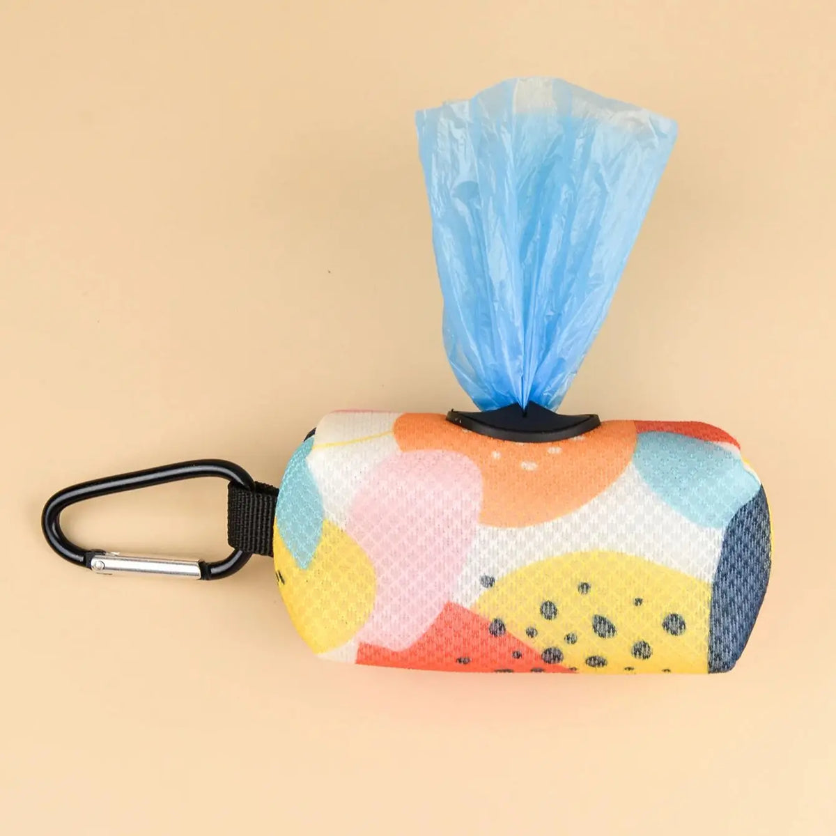 A colorful poop bag dispenser with a patterned fabric and a blue plastic bag attached to a black clip.