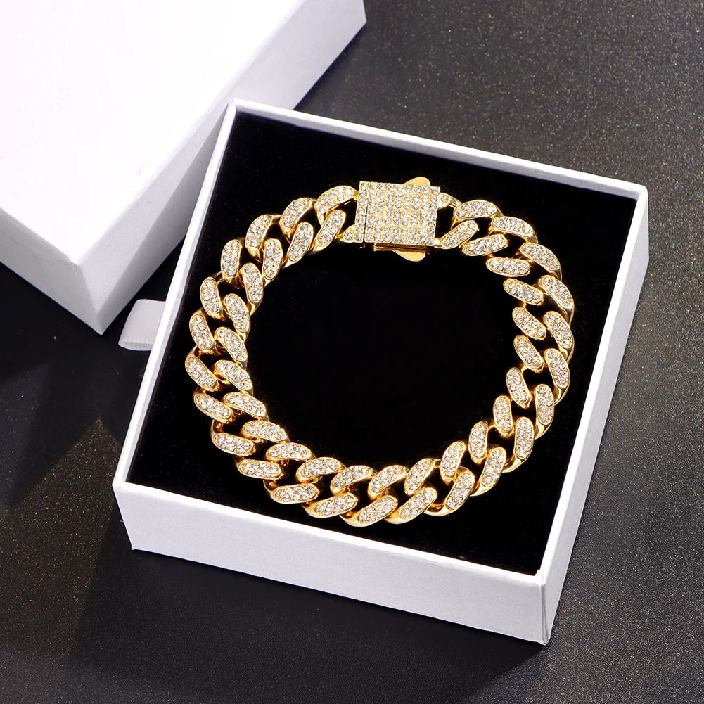 A gold iced out Cuban link bracelet with rhinestone accents displayed in a white jewelry box.