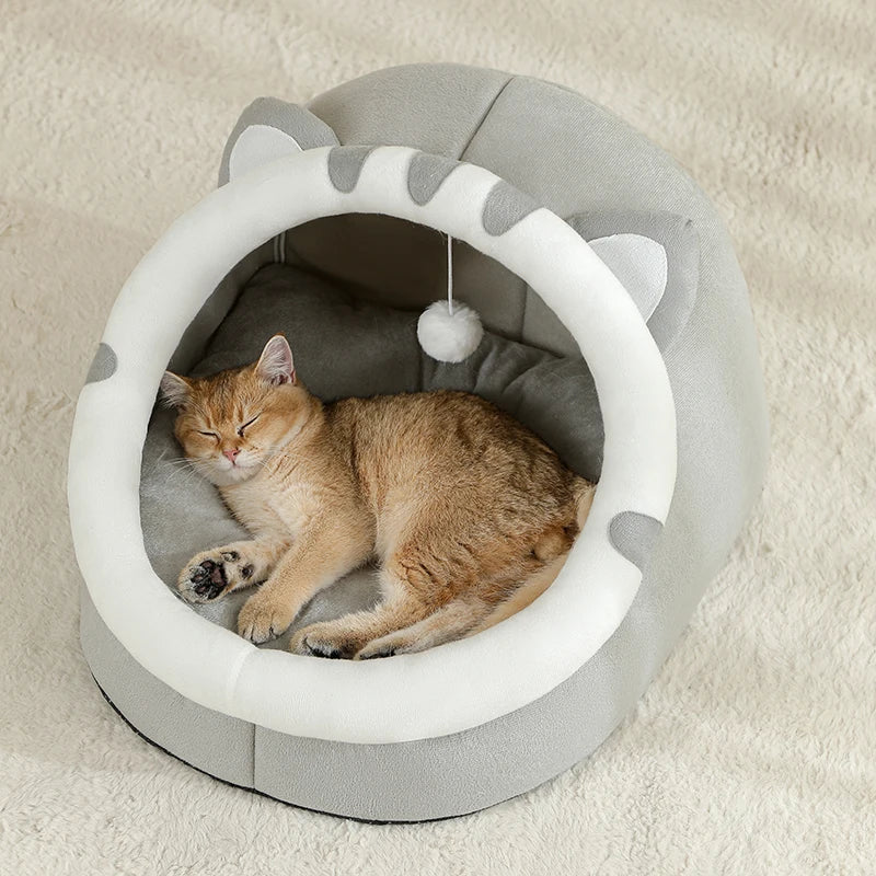 Un gato naranja atigrado esponjoso relajándose dentro de una cama para mascotas redonda de color gris claro con un borde blan