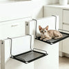 A tabby kitten is resting in a black mesh hammock mounted on a white cabinet door.