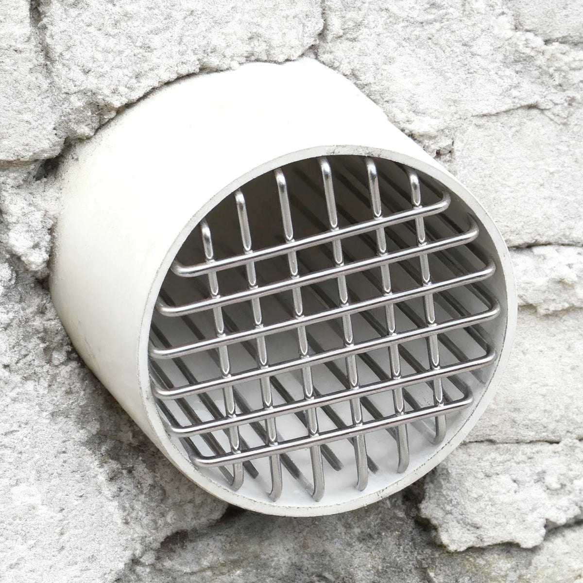A round stainless steel roof and floor drain mesh cover set against a rough stone wall.