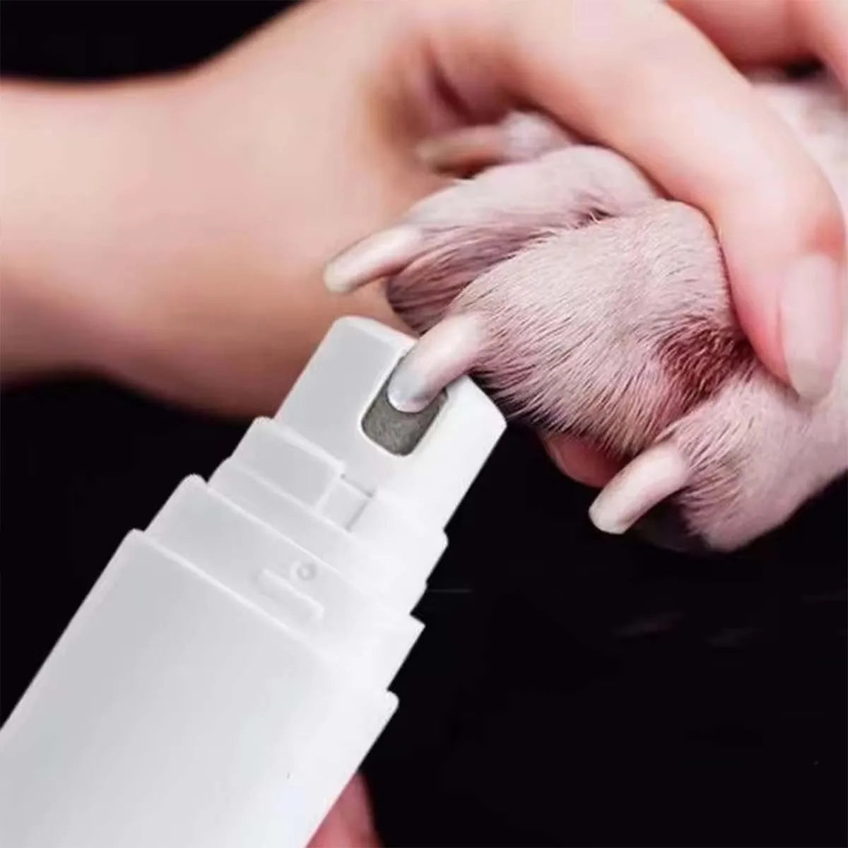 A hand is holding a pink pet paw while using a white electric nail grinder tool for grooming.