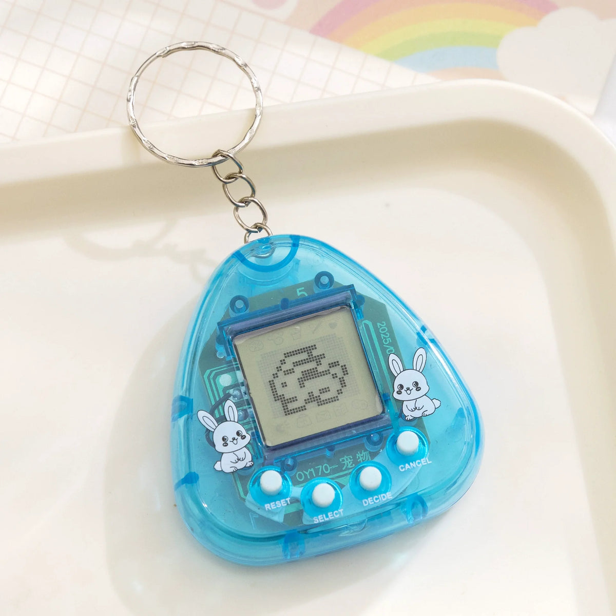 A clear blue digital pet toy with a silver keyring is placed on a white tray.