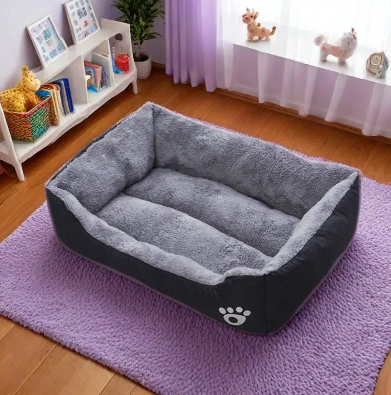 A gray and black plush dog bed is placed on a purple rug indoors near a window.
