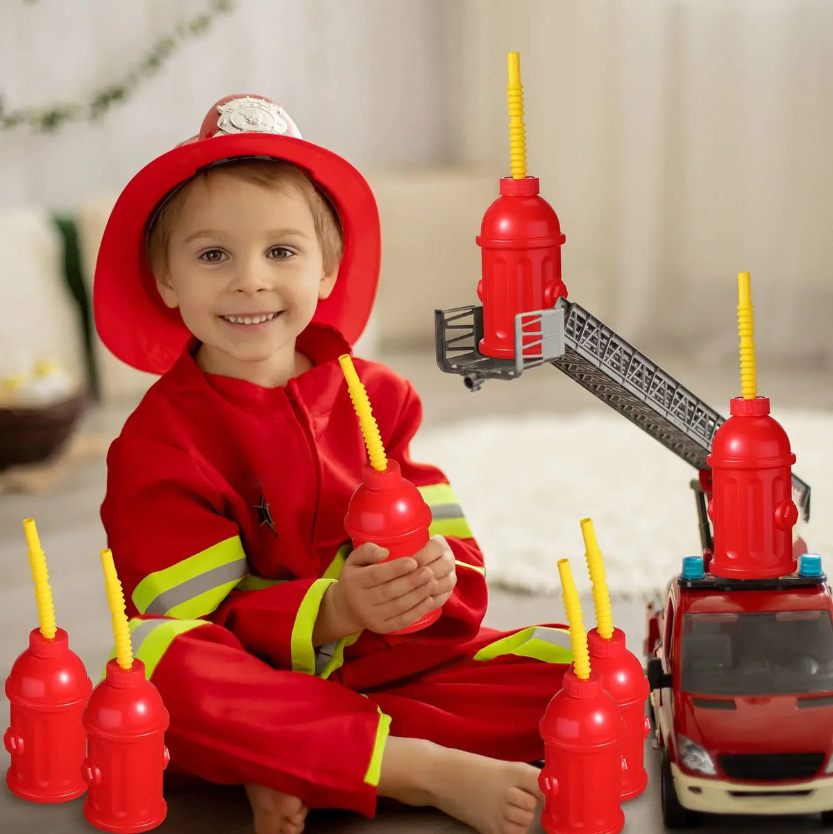 A smiling child is holding a red fire hydrant straw cup with a yellow straw and lid, set against a blurred background.