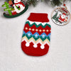 A knitted red winter dog sweater featuring geometric patterns and white pom-poms, displayed next to a Christmas ornament.