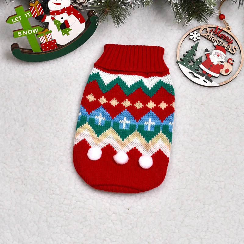 A knitted red winter dog sweater featuring geometric patterns and white pom-poms, displayed next to a Christmas ornament.