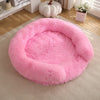 A round, fluffy pink dog bed with a removable cover resting on a light beige carpet.