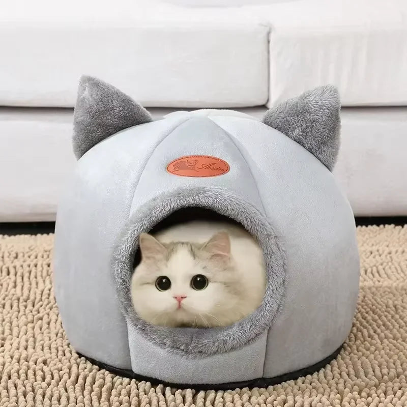 Un lit-nid en peluche gris avec une entrée pour un petit chaton blanc.