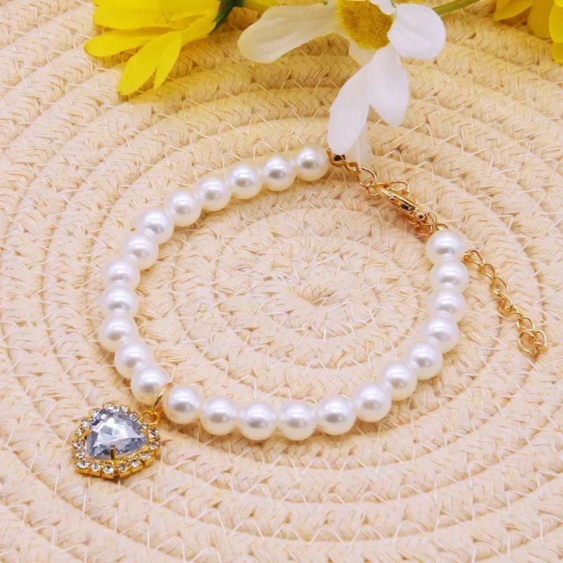 A gold pearl necklace with a clear gemstone pendant rests on a light beige textured surface.