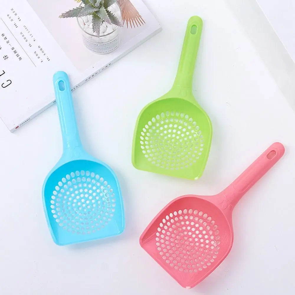 Three plastic cat litter scoops in blue, green, and pink are displayed on a white surface.