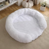 A round, ultra-soft white dog bed with a fluffy, removable cover resting on a light beige rug.