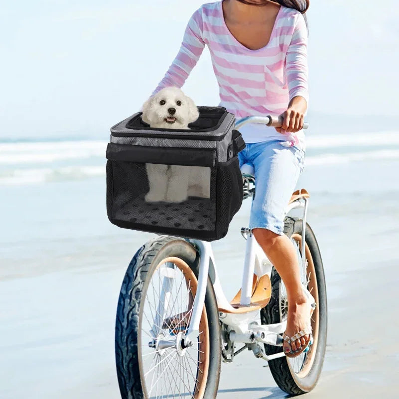 Une personne chevauche un vélo pliable avec un panier portant un petit chien blanc sur une plage.
