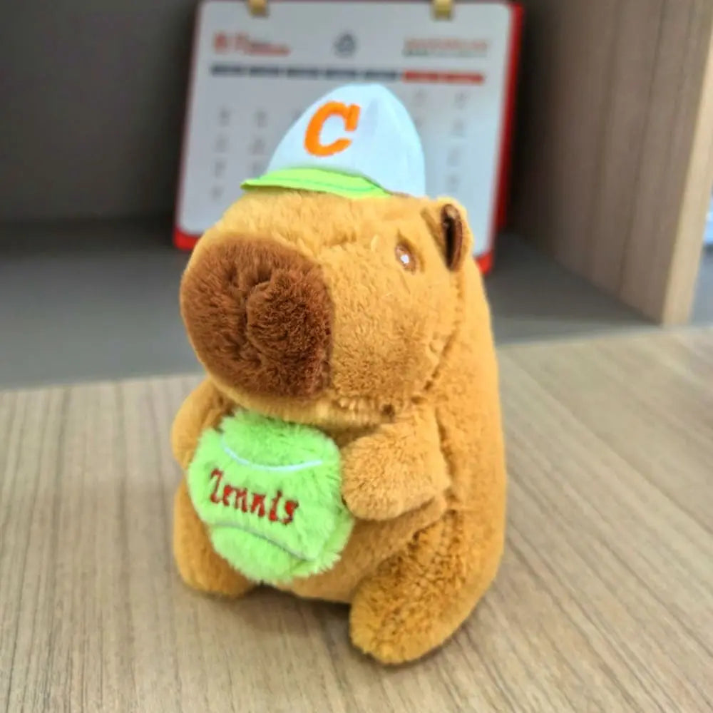 Orangefarbene Capybara-Plüschpuppe mit grünem Hoodie und weißer Baseballkappe mit orangefarbener C