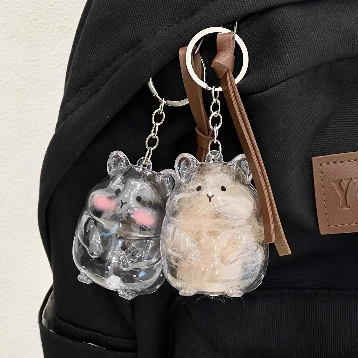 Clear glass hamster figurine keychain with a fluffy white charm hanging from a leather strap