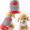 Un chien duveteux portant un gilet rayé rouge et blanc avec un nœud rouge et des accents dorés.