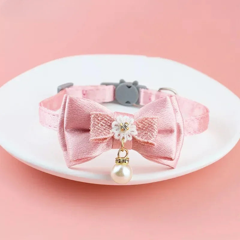 Pink lace bow cat collar with a bell and pearl bead charm displayed on a white plate.