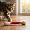 A tabby cat is interacting with a red and white foam cat toy on a wooden floor.