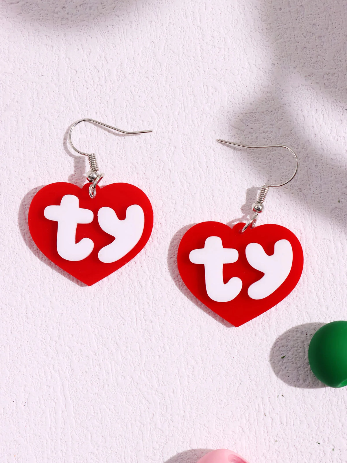 Pair of red acrylic heart stud earrings with white initial letters ty