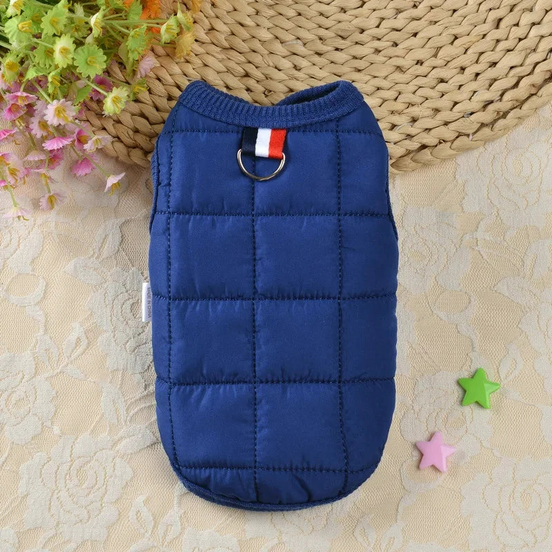 Manteau de chien bleu marine rembourré avec un charm de drapeau rouge et blanc sur une surface beige.