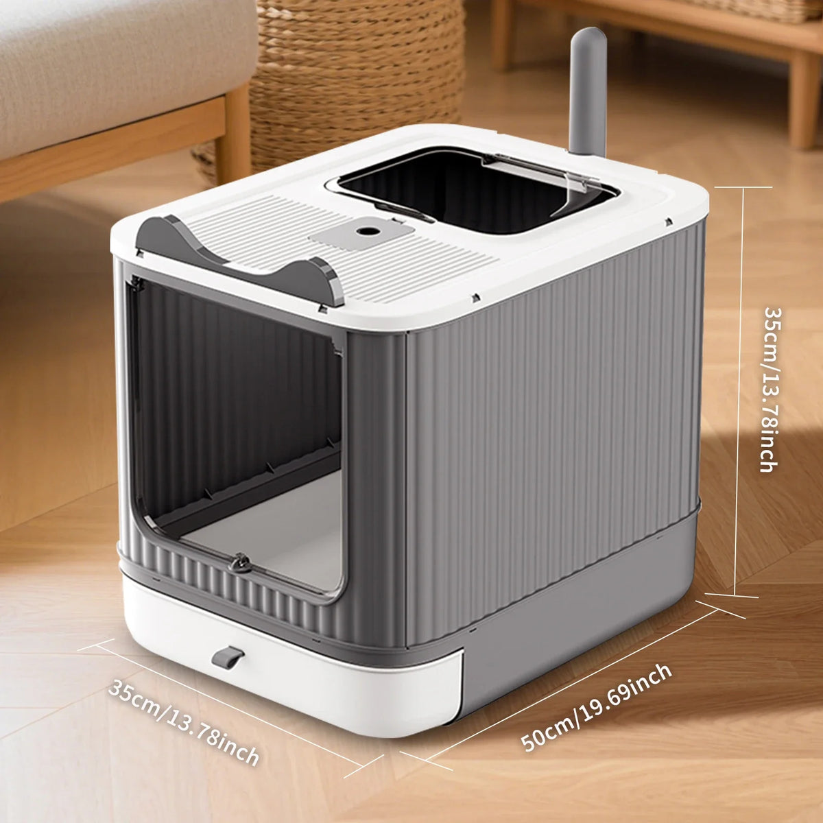 A gray and white enclosed stainless steel cat litter box with a lid and a vertical drain pipe is shown on a wooden floor.