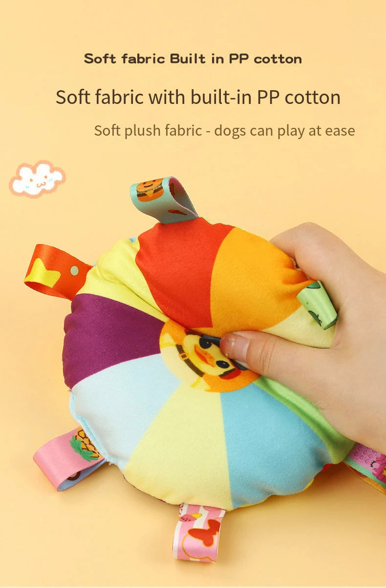 A hand is holding a colorful plush dog toy shaped like a flying disc, made with soft fabric and built in PP cotton.