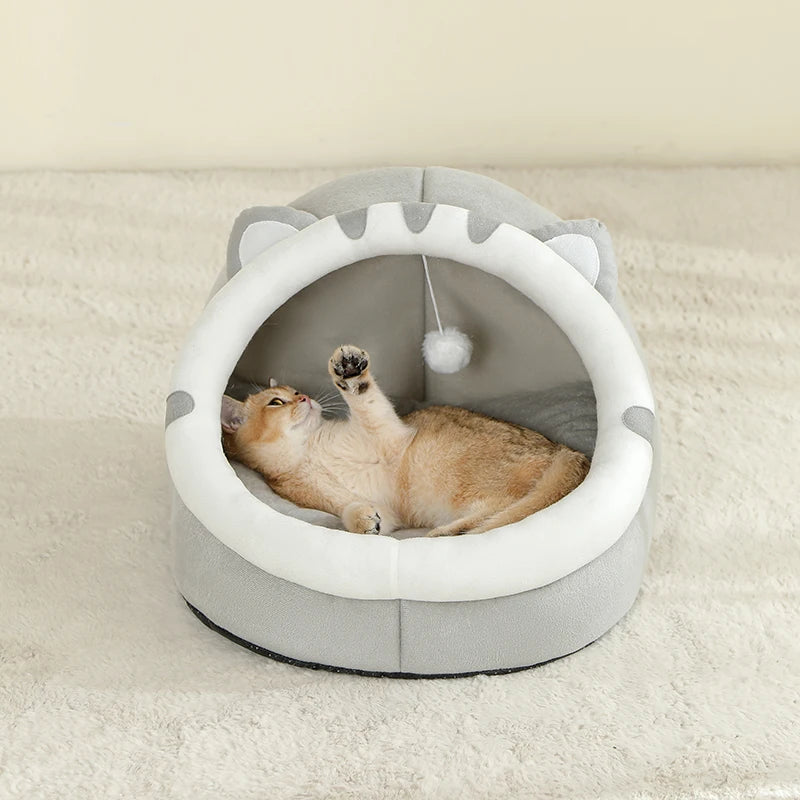 A fluffy orange cat is relaxing inside a gray, arched pet bed with white interior lining.
