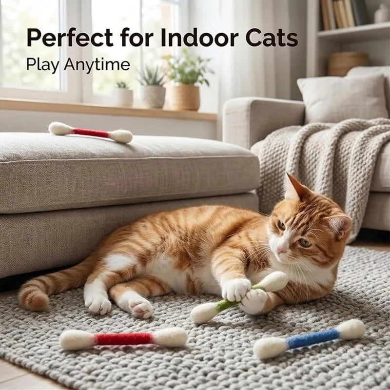 A tabby cat is playing with felt chew sticks on a gray rug indoors.